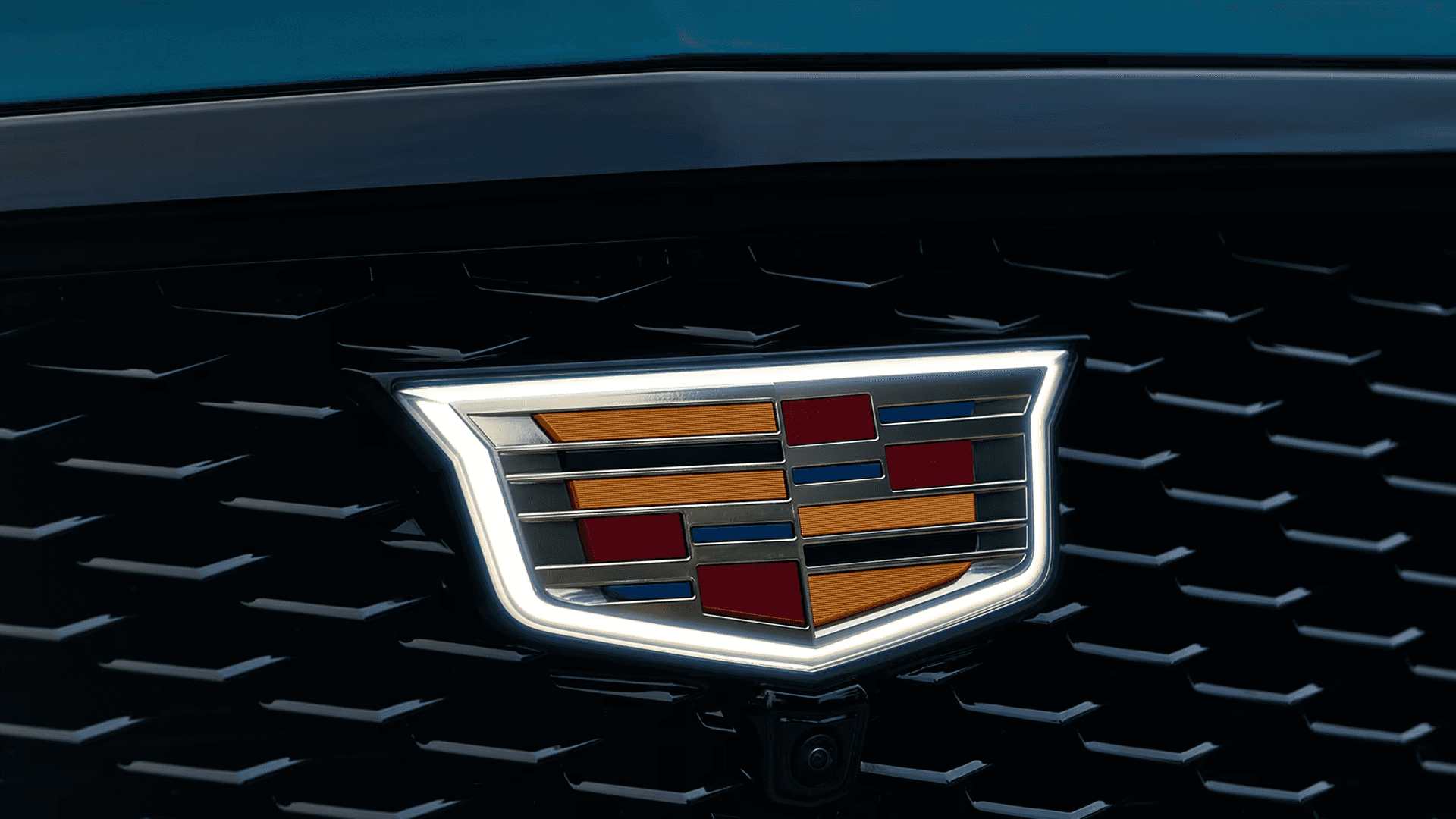 Close up of illuminated Cadillac crest logo centered in black grille with surrounding LED outline and camera below emblem