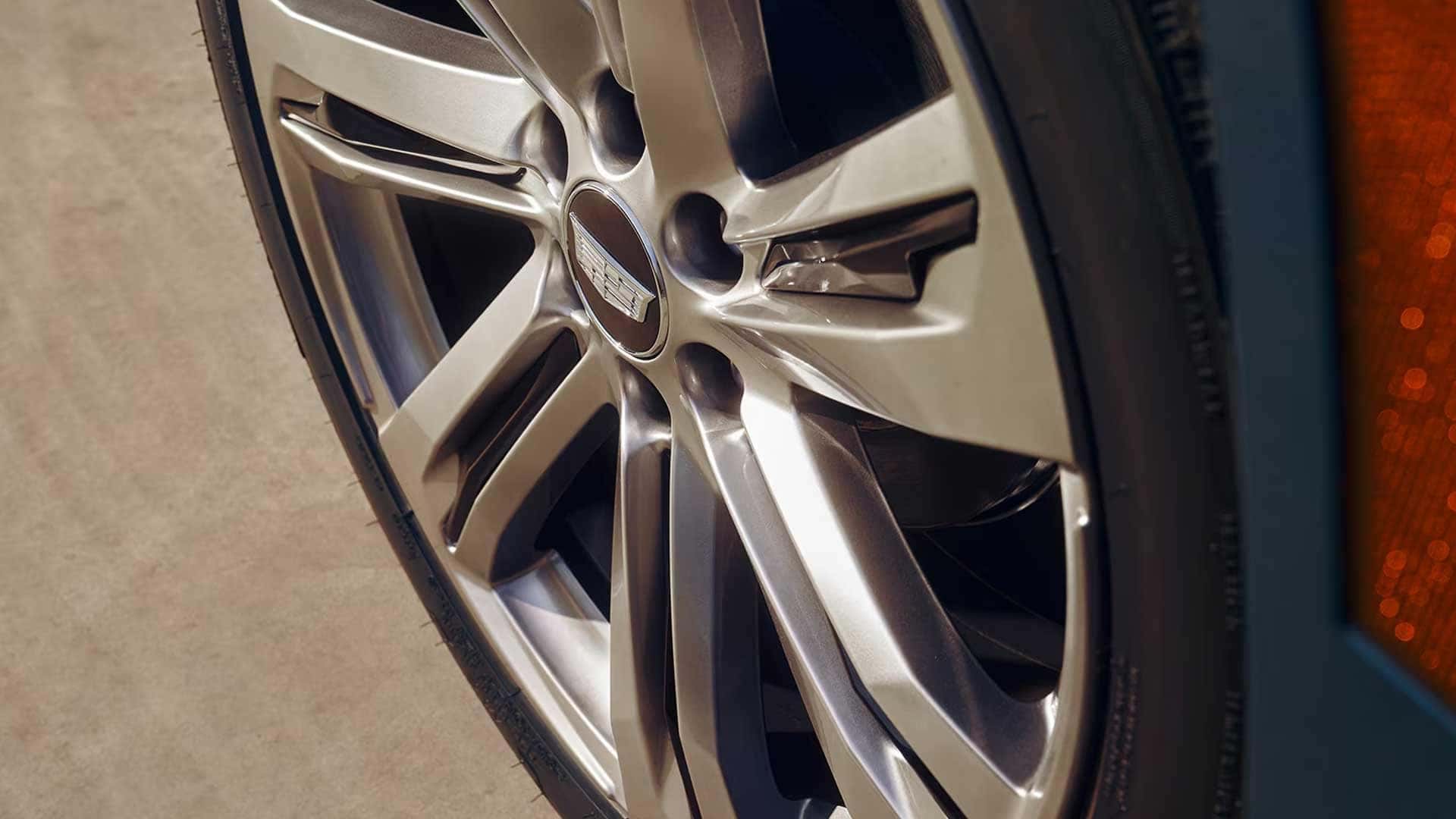 Close up of Cadillac alloy wheel with multi spoke design and center cap logo, tire and brake components partially visible