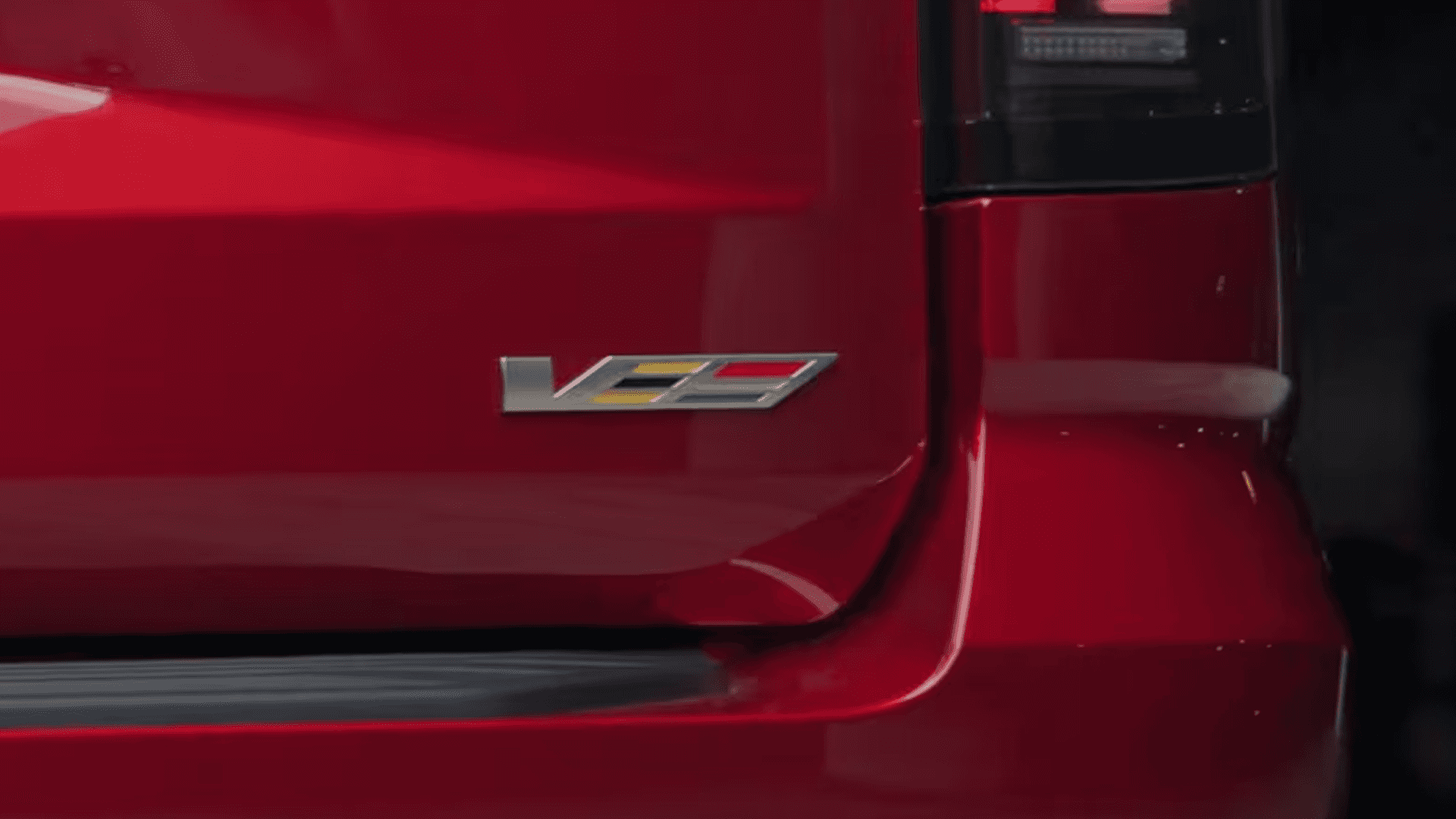 Close up of V-Series badge on red Cadillac Escalade tailgate next to vertical taillight with glossy paint reflections