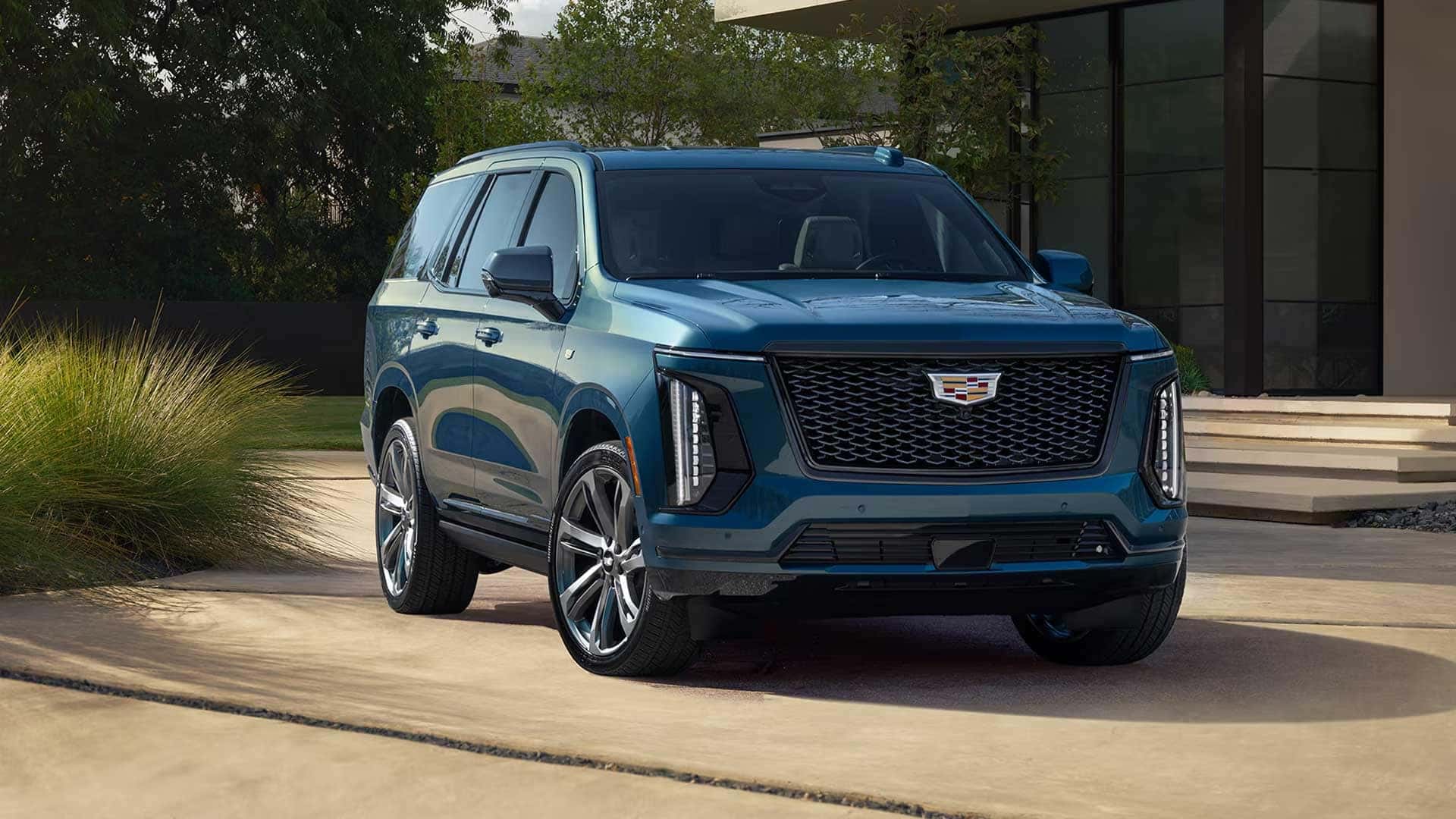 Blue Cadillac Escalade parked in front of a modern home with trees and landscaping nearby