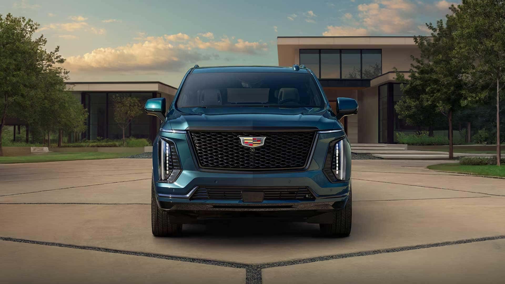 Blue Cadillac Escalade shown from the front in a driveway outside a modern building