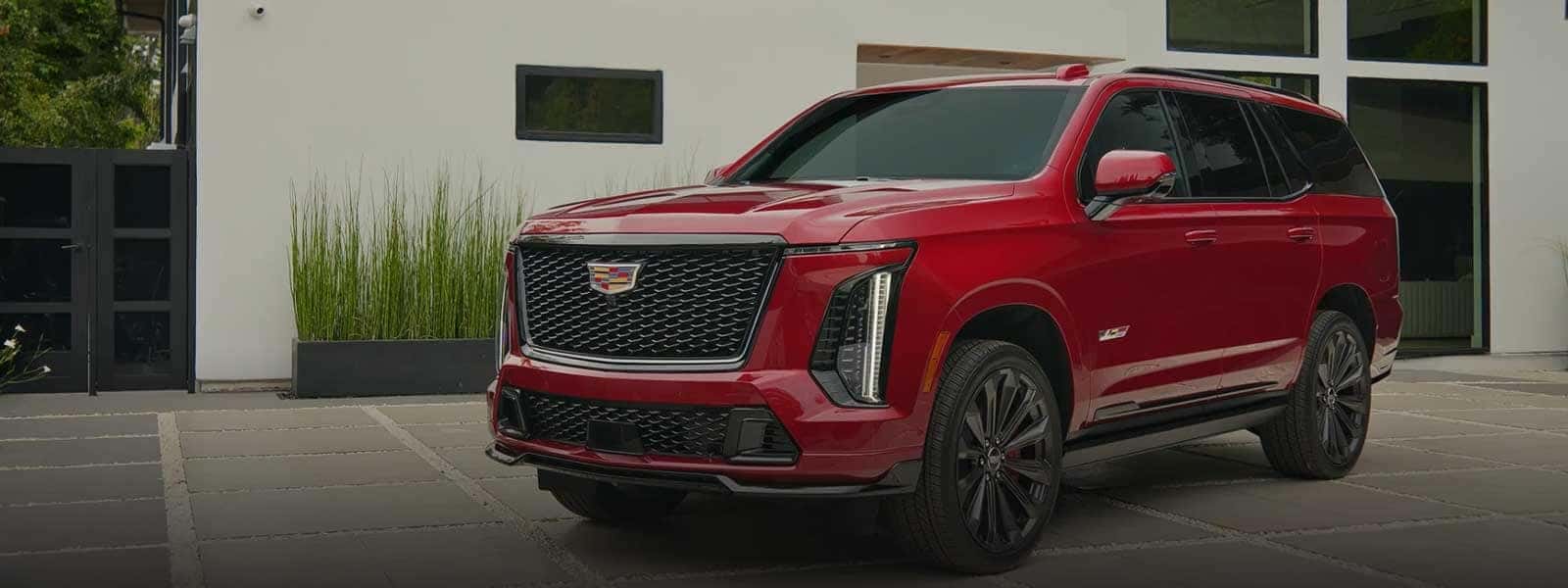 Red Cadillac Escalade parked outside a modern building with dark grille and vertical lights