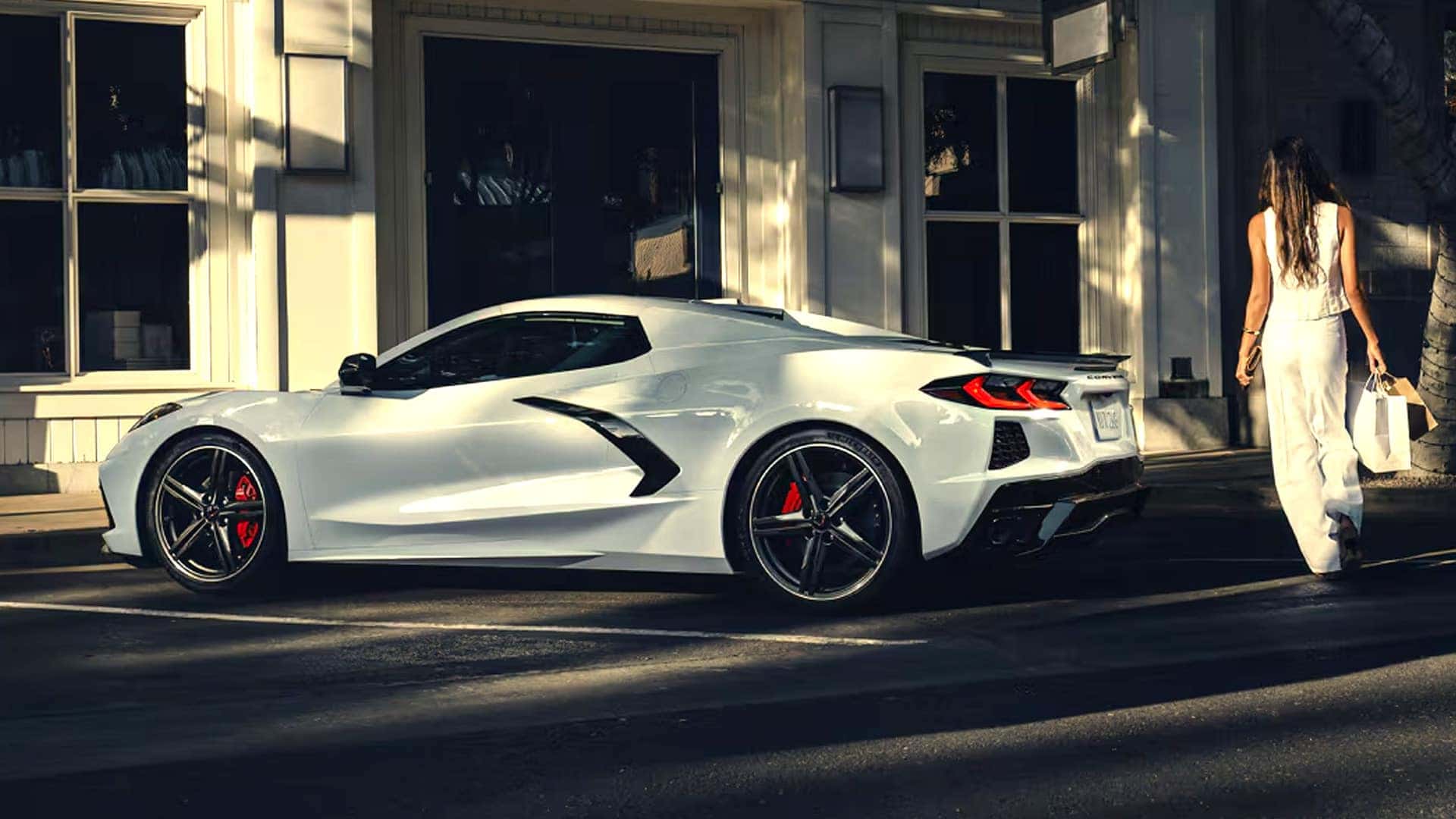White Corvette coupe parked at curb with black side intake, black wheels, and red brake calipers.