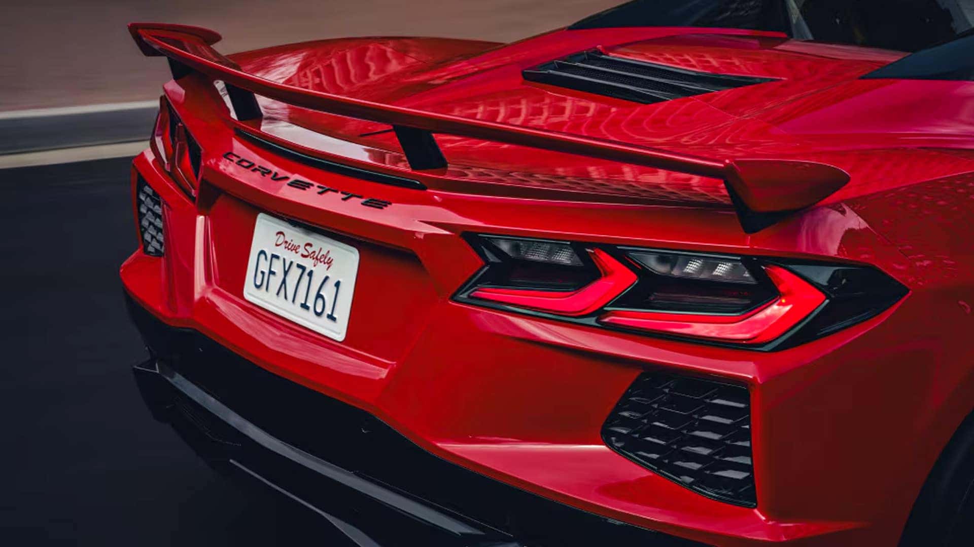 Close-up of a red Corvette rear section with spoiler, taillights, license plate, and black vents.