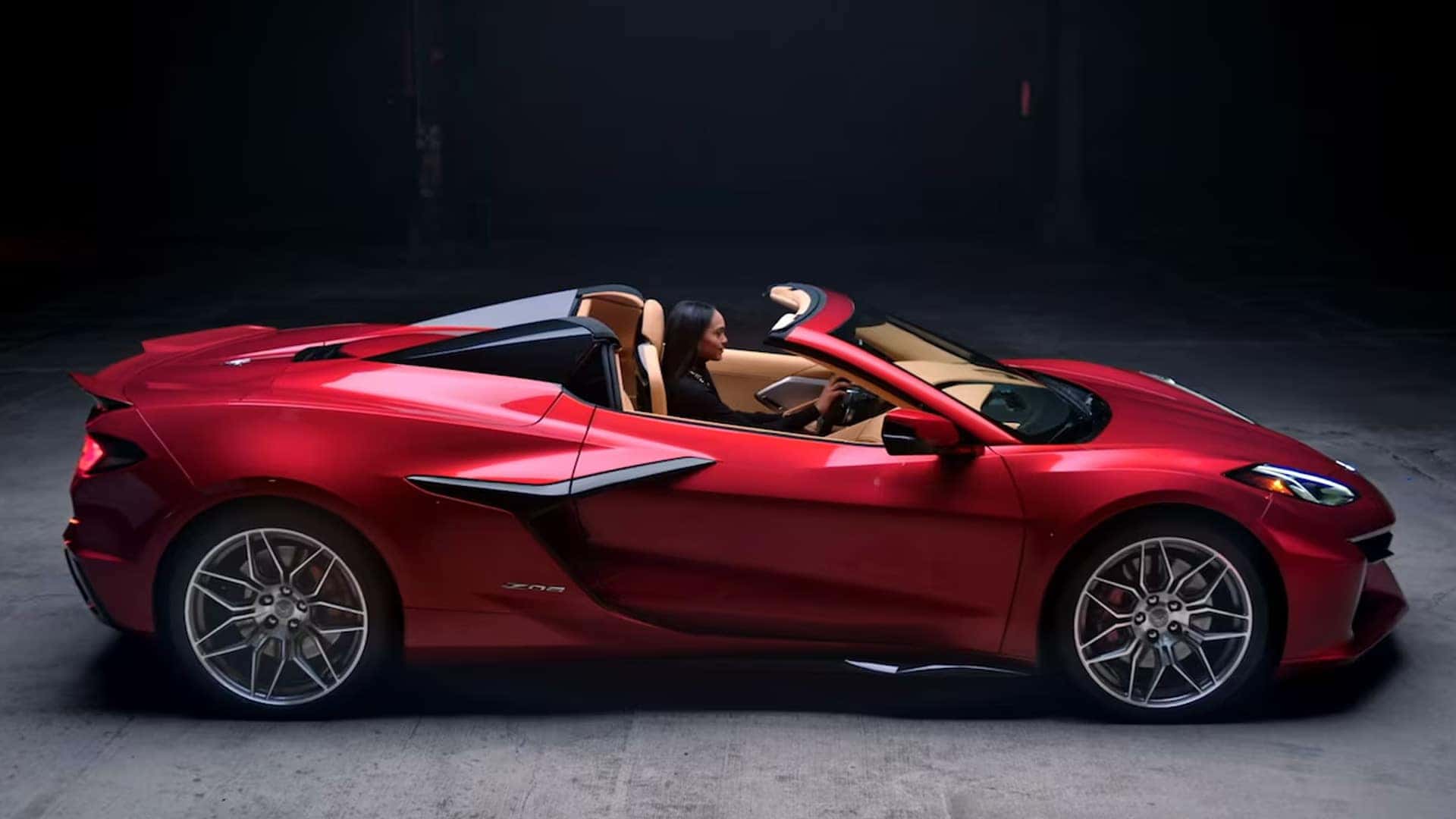 Red Corvette convertible shown from the side with the top down and a driver inside.