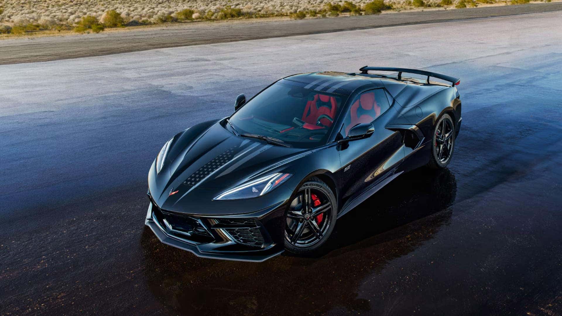 Black Corvette coupe with striped hood graphics, red seats, rear wing, and black wheels.