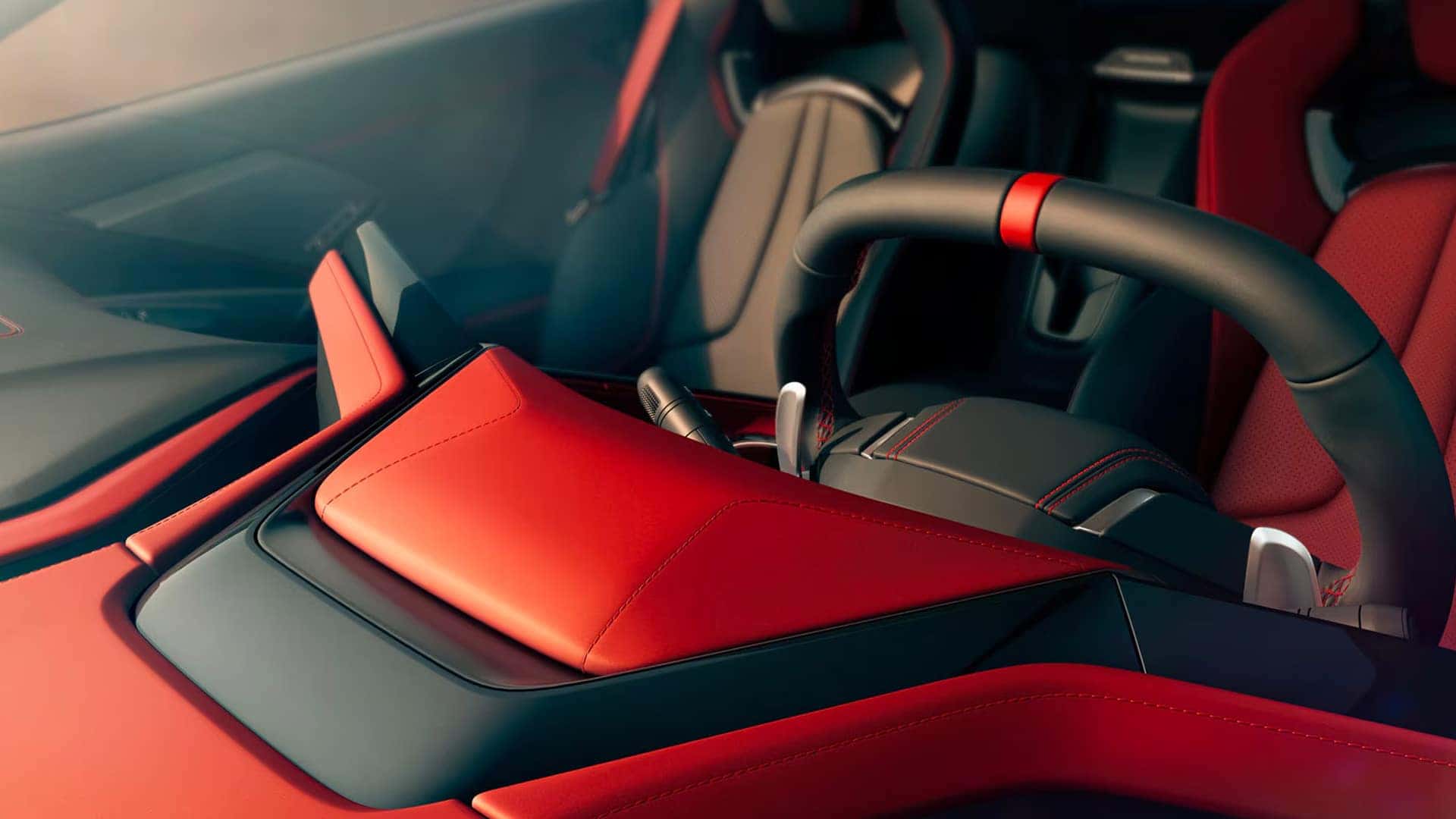 Close view of red and black car interior with seats, steering wheel, center console, and stitching