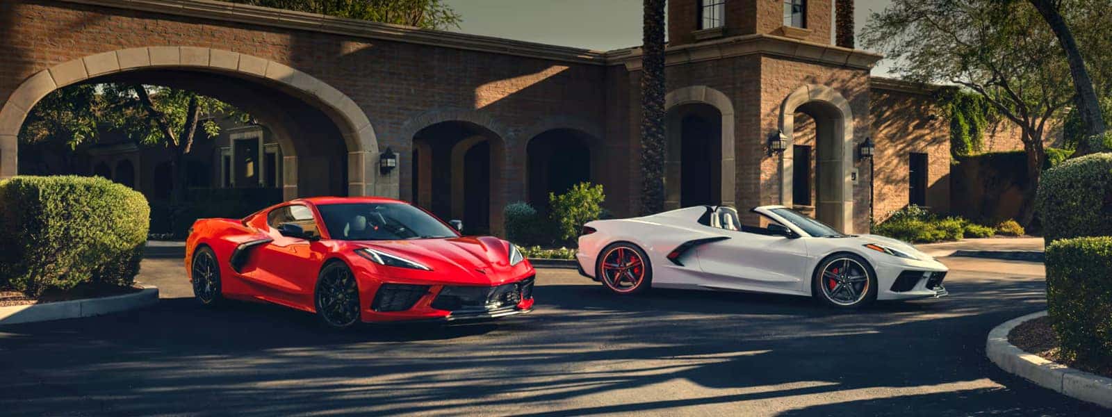 A red and a white Corvette Stingray parked outside a brick building with arched entryways