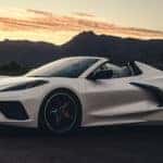 White Corvette convertible shown in profile with the roof open against a mountain sunset background.