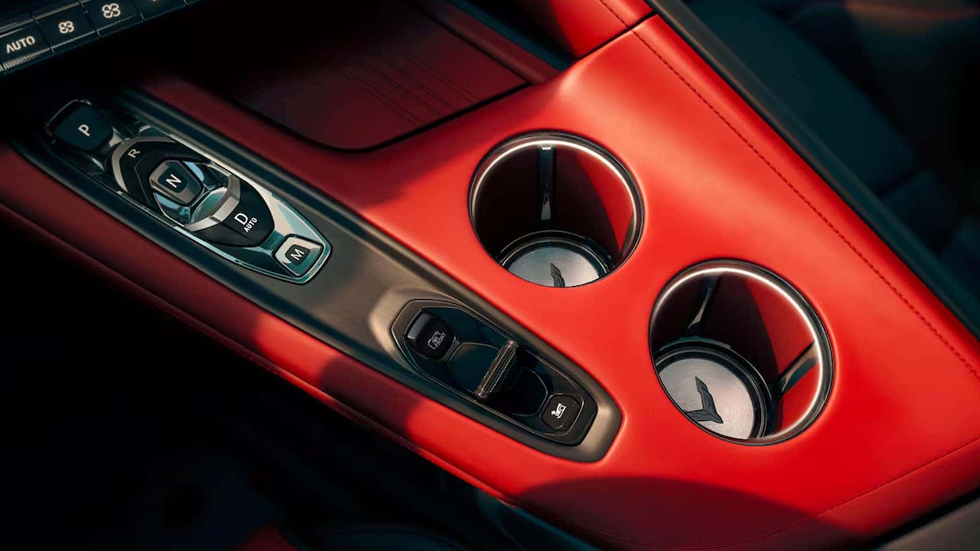 Close-up of Corvette center console showing gear buttons, drive controls, cupholders, and red trim.