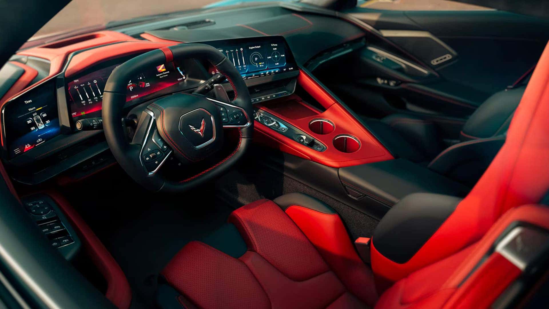 Corvette cockpit with red seats, steering wheel, digital displays, center screen, console, and cupholders.