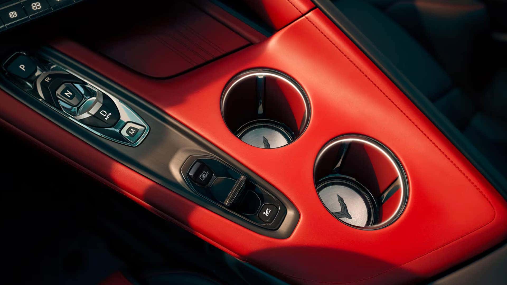 Close view of a red Corvette center console with gear buttons, cupholders, and drive control switches.