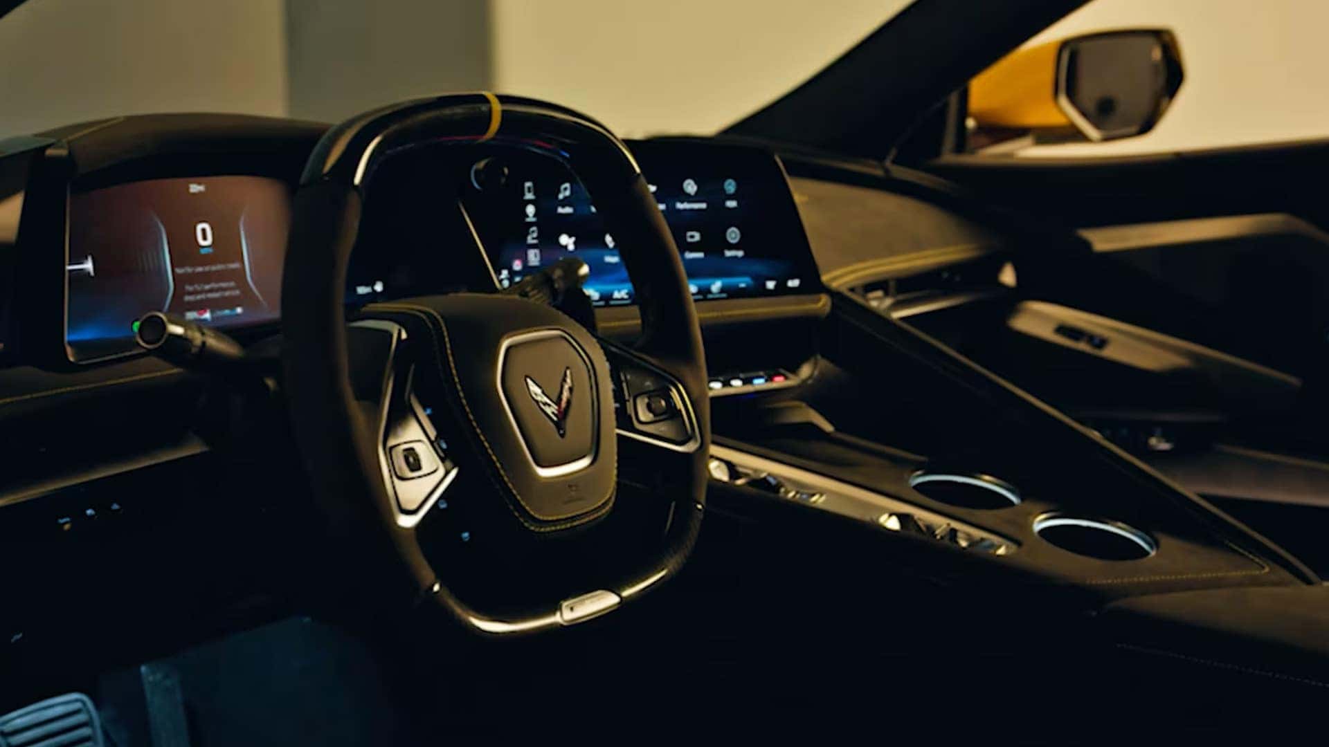 Dark Corvette cockpit with steering wheel, digital gauge screen, center touchscreen, console, and cupholders.