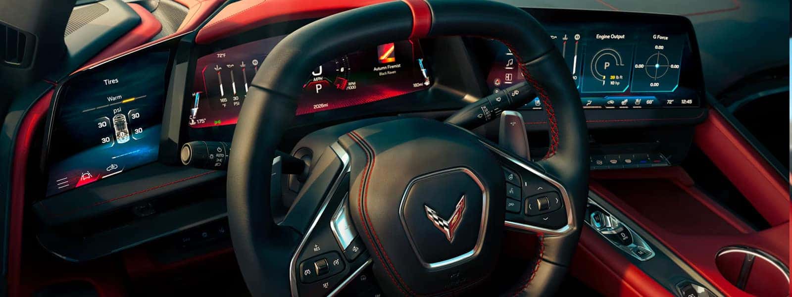Wide Corvette cockpit view with steering wheel, three digital screens, red console, and cupholders.
