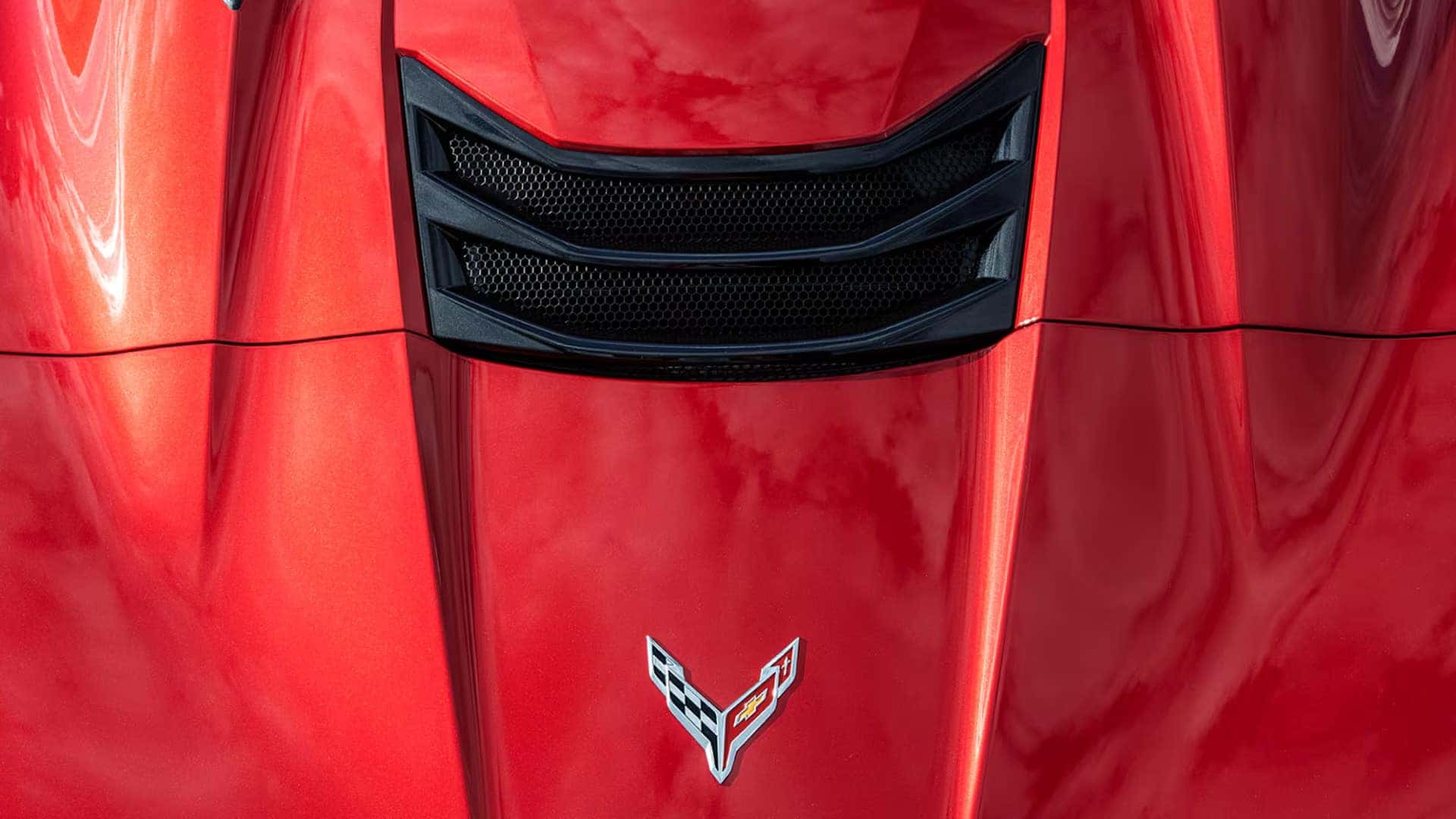 Close-up of a red Corvette hood with black vent openings and the Corvette crossed flags emblem.
