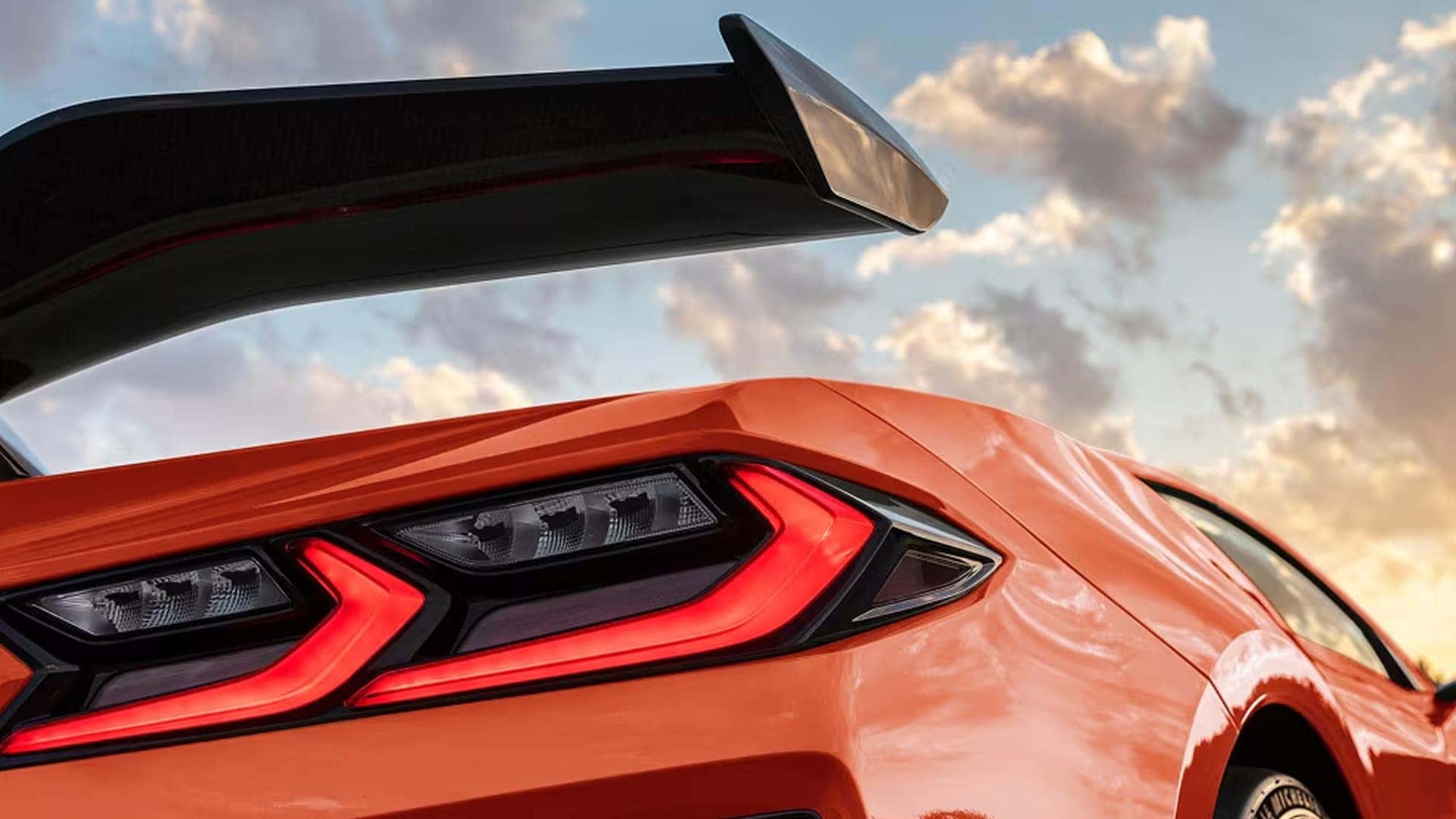 Close-up of an orange Corvette rear section showing the taillight, large wing, and rear bodywork.