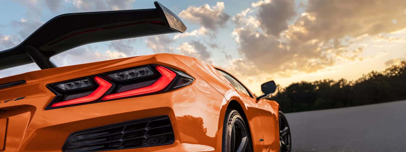 Close-up of an orange Corvette rear corner showing the taillight, rear wing, and black vent trim.