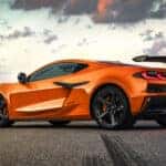 Side profile of orange Corvette Z06 parked on pavement showing rear wing, quad exhaust, and sculpted body lines