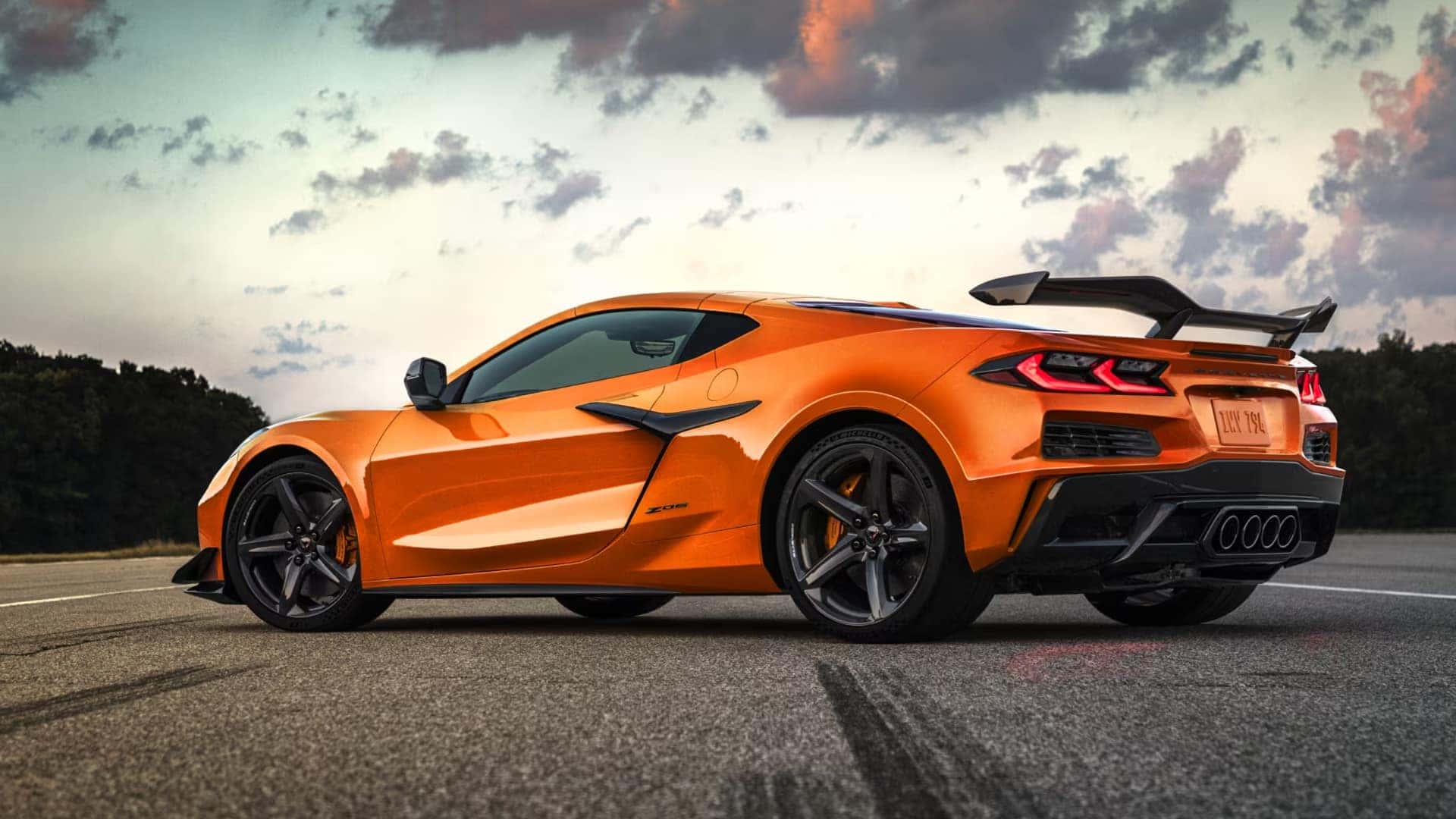 Side profile of orange Corvette Z06 parked on pavement showing rear wing, quad exhaust, and sculpted body lines