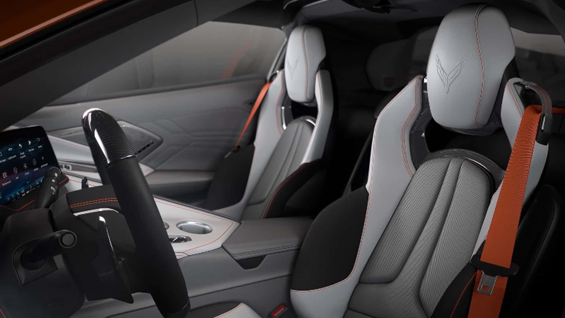 Side view of the 2026 Corvette Z06 showing both sport bucket seats in gray with orange stitching and seatbelts, the carbon fiber gear selector, and center console.