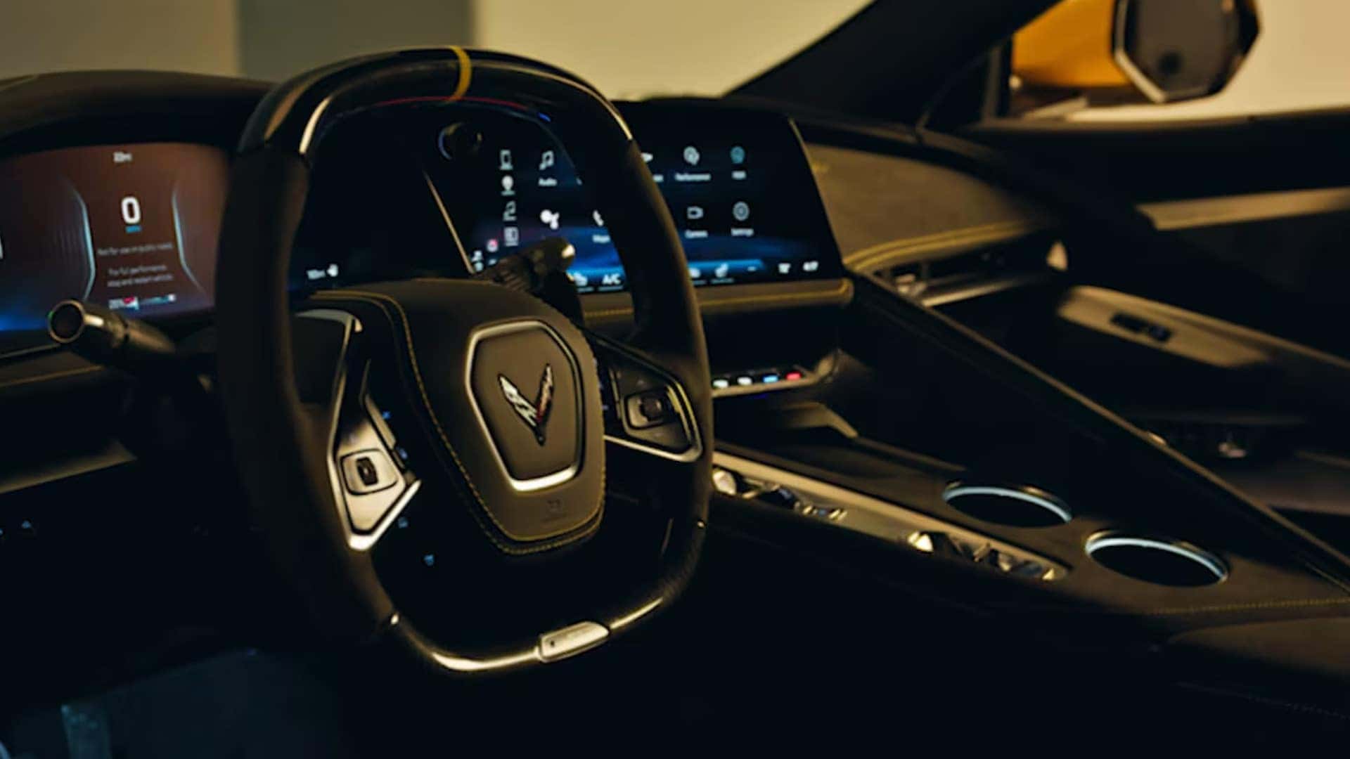 Dim interior view with steering wheel, digital display, center touchscreen, console, and cupholders.