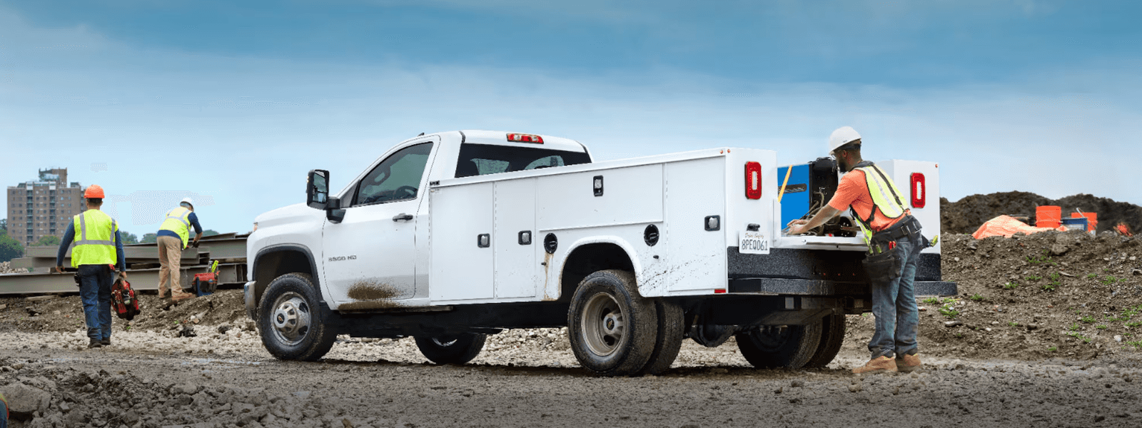 White Silverado 3500 HD utility truck parked on a dirt construction site with workers and tools in the background