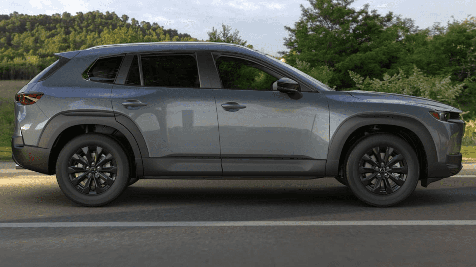 Side profile of a gray Mazda CX-50 on pavement, showing black wheels, dark trim, and tinted windows