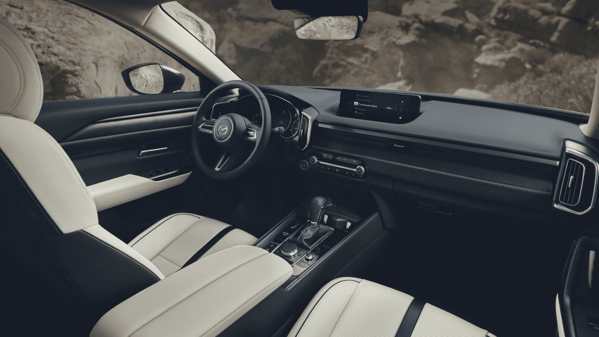 Front cabin view with light seats, black dashboard, center display, console controls, and rocky scenery outside