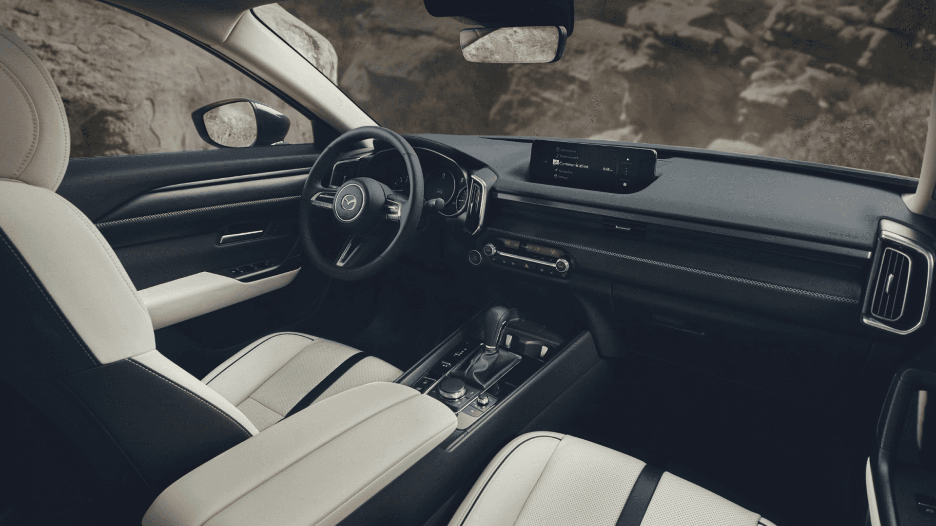 White front seats and dashboard with center display, steering wheel, console controls, and rocky background outside
