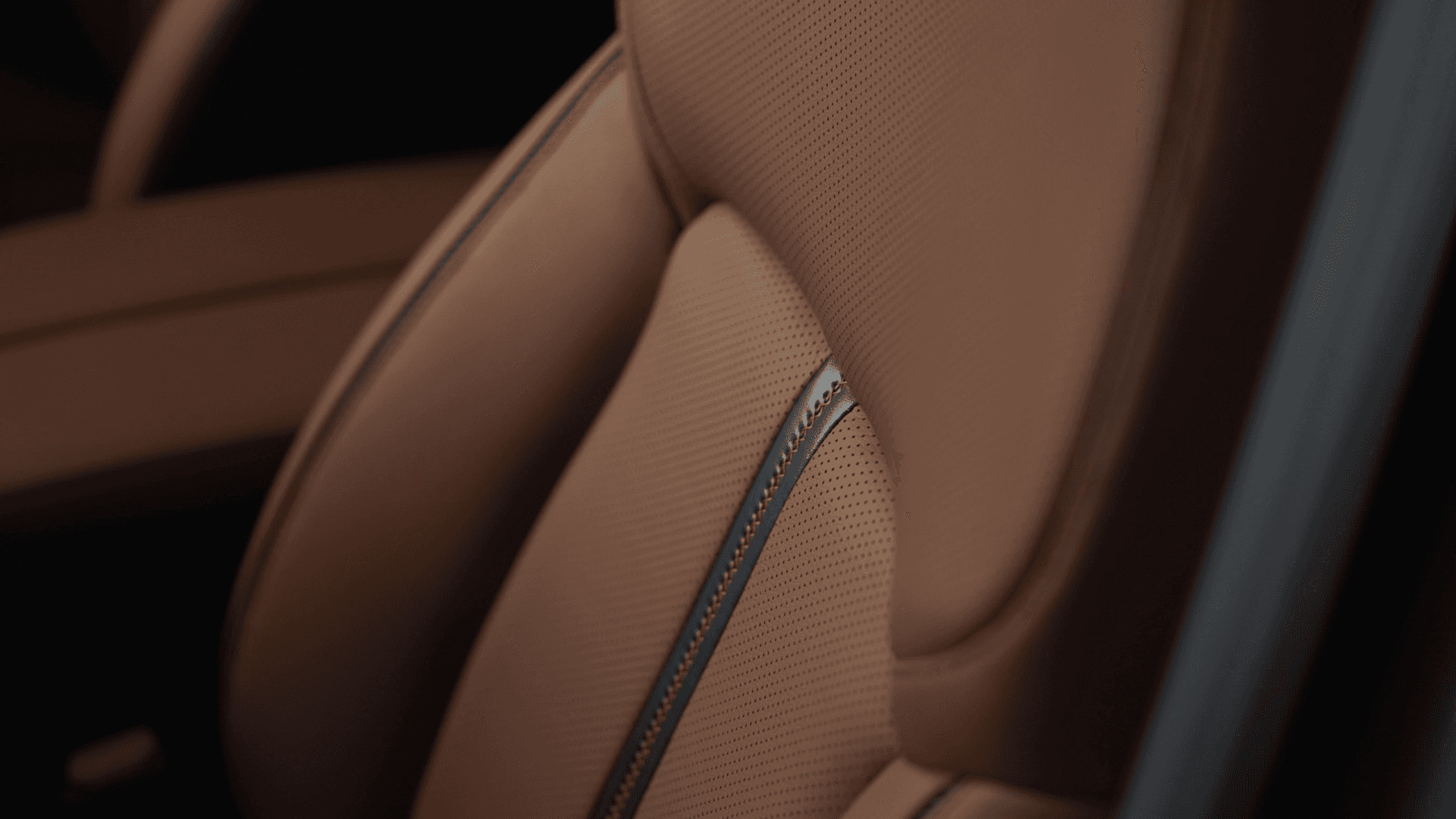 Close-up of a brown perforated seat with black accent stripe and visible contrast stitching along the center