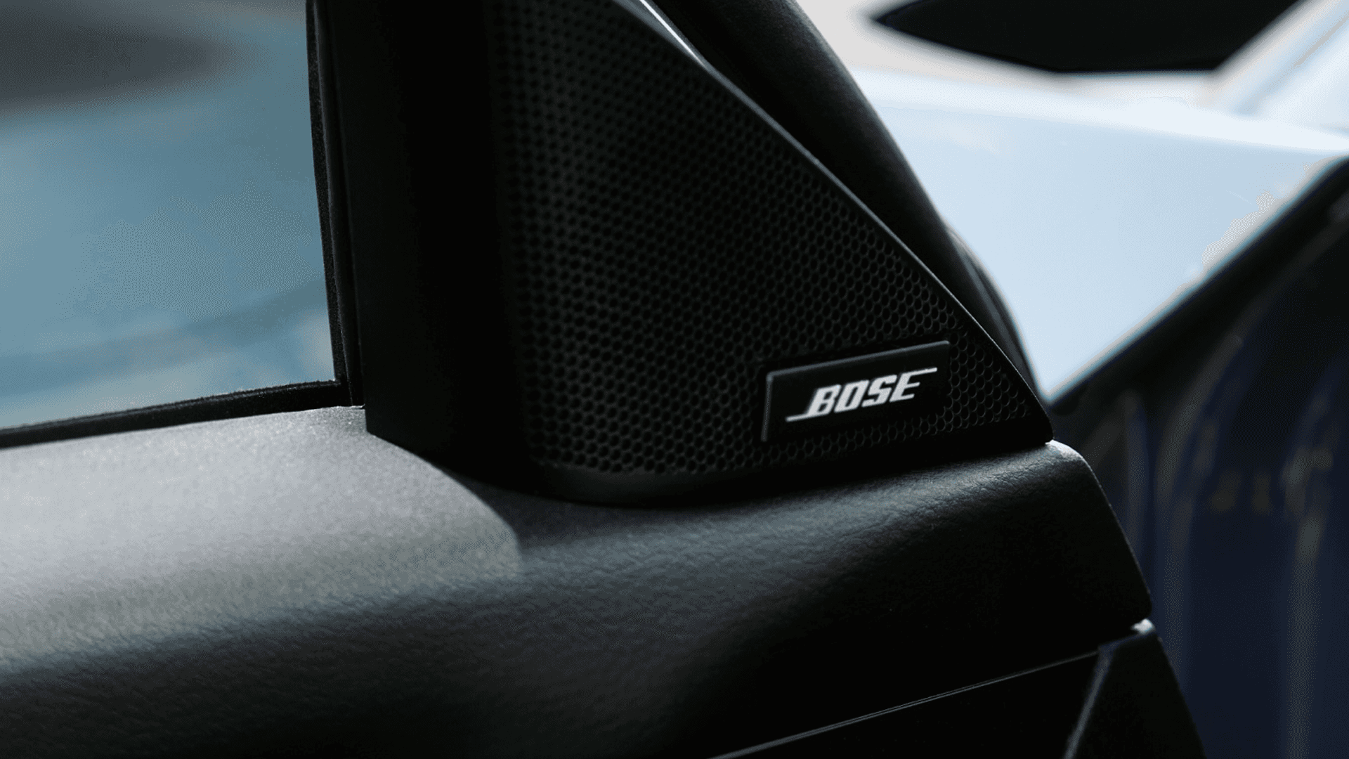Close-up of a Bose speaker mounted near the front door pillar with part of the side mirror in the background