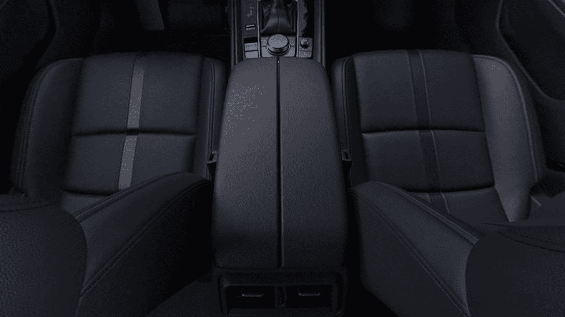 Top-down view of two black front seats, center armrest, rear air vents, and center console controls