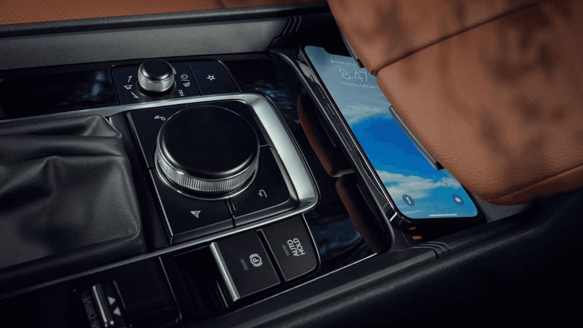 Center console controls beside a smartphone resting in a storage tray under a brown leather armrest.