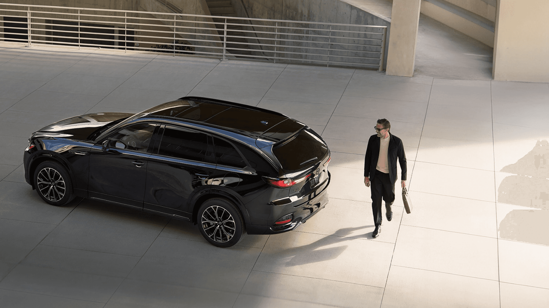 High-angle view of a black Mazda SUV parked in a concrete lot with a person walking nearby casting a shadow