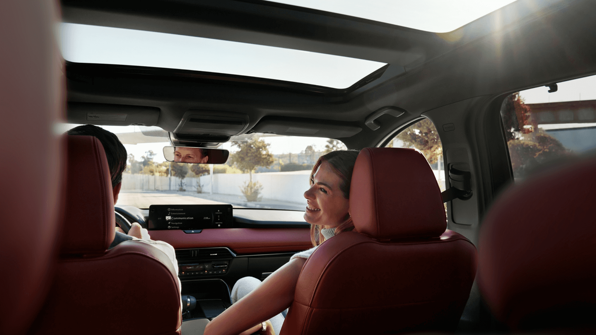 Interior view with red seats, panoramic moonroof, center display, and two people visible from the back seat