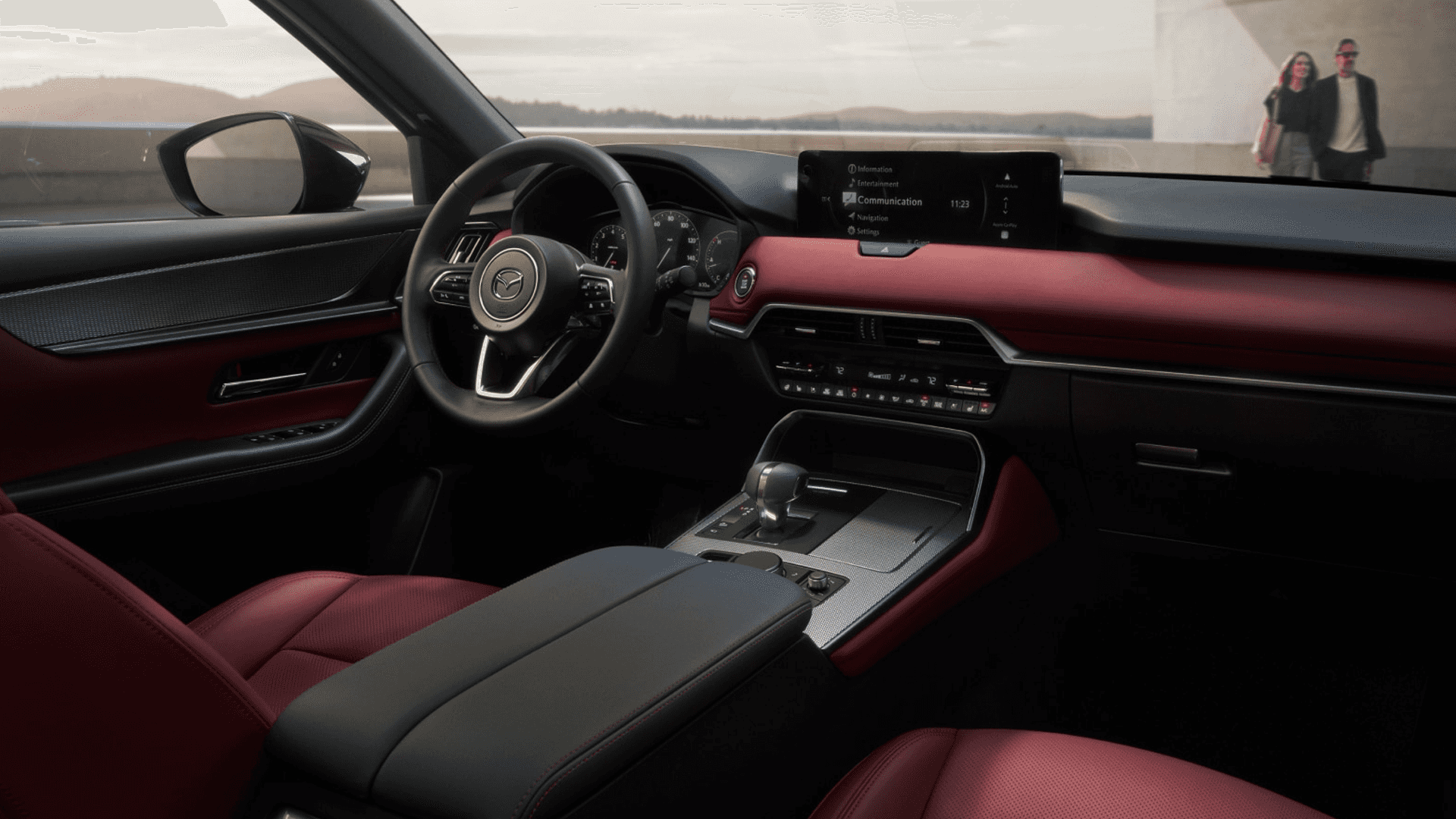 Driver view of dashboard with center display, steering wheel, console controls, and red interior trim