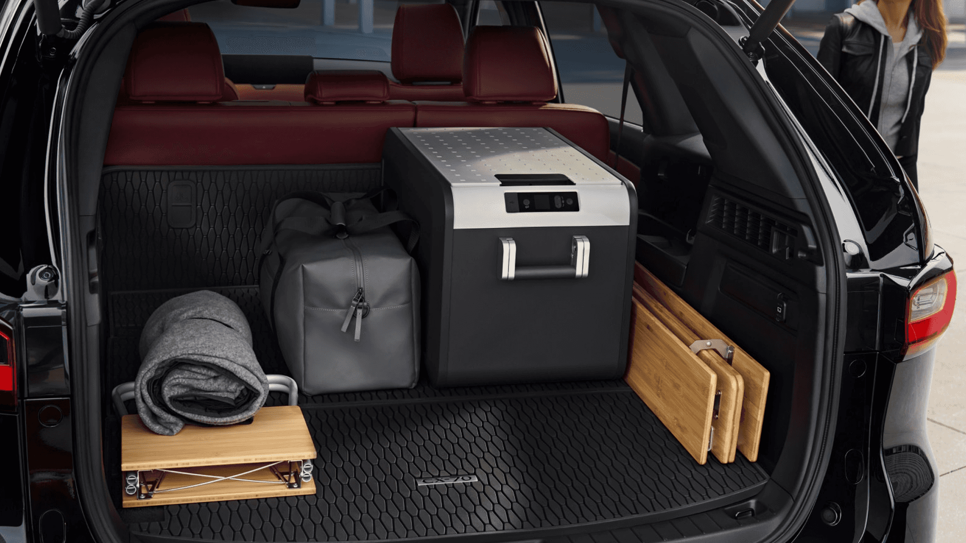 Open rear cargo area with bags, folded tables, blanket, and storage compartment inside the vehicle
