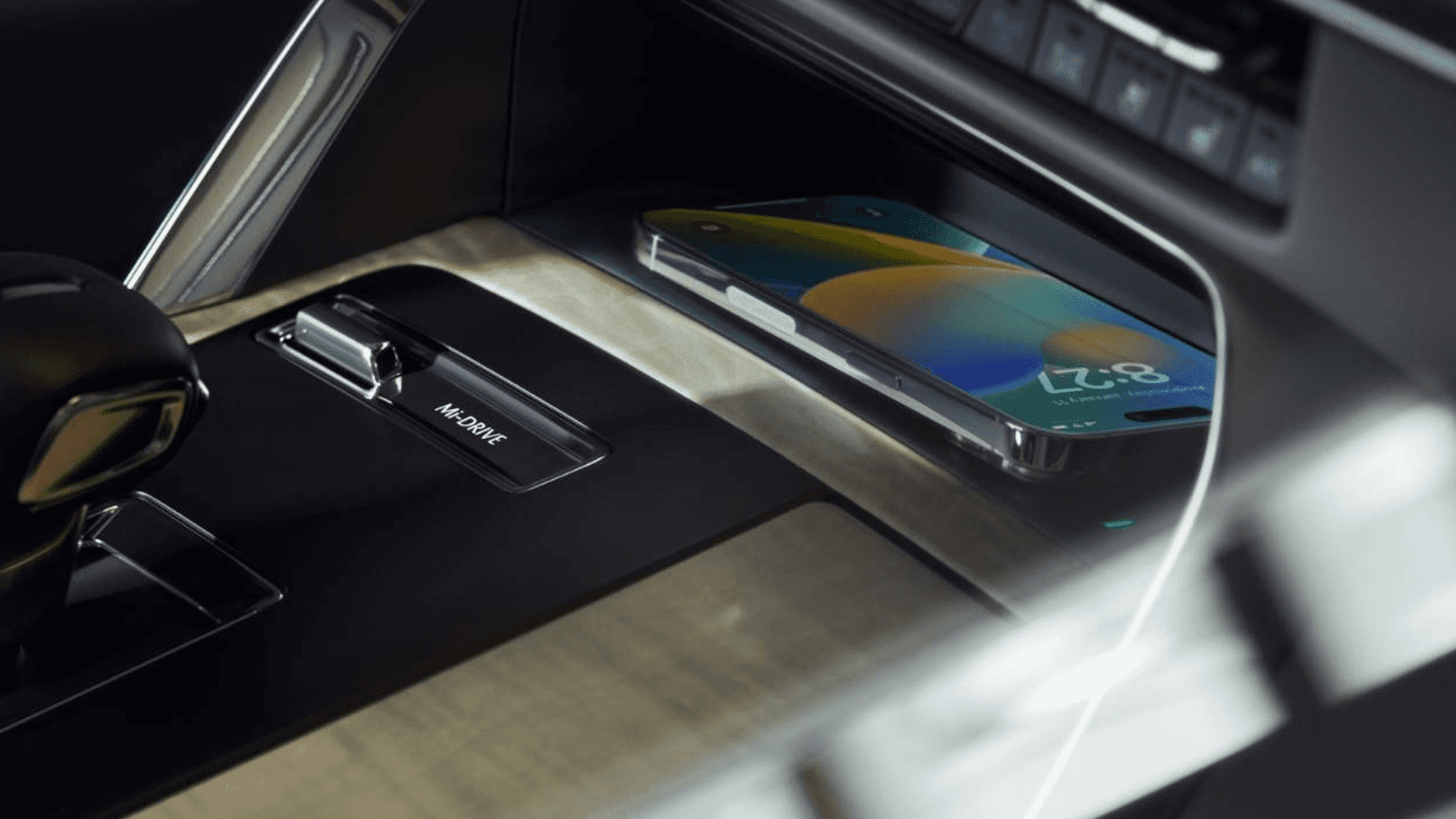 Center console with gear selector and wireless charging pad holding a smartphone, surrounded by metallic trim.
