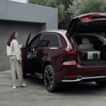 Red 2026 Mazda CX-90 with rear liftgate open showing luggage in cargo area and two people standing beside the vehicle