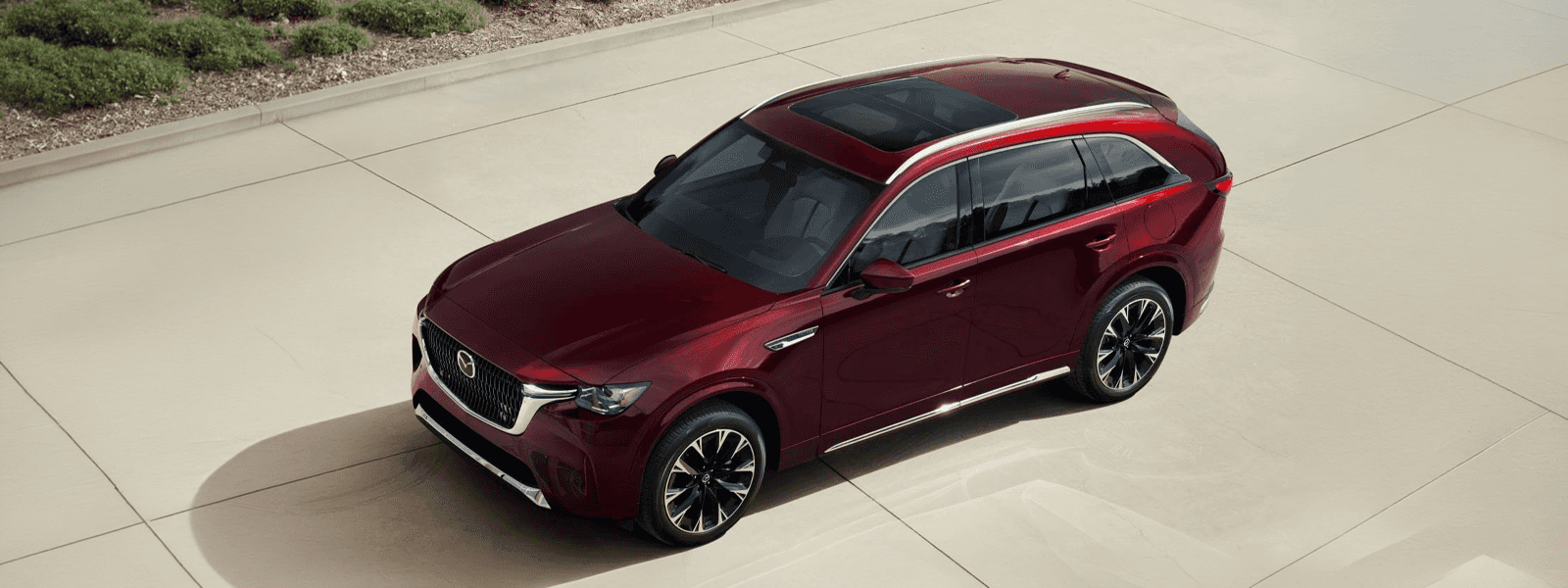 Red 2026 Mazda CX-90 from above showing panoramic glass roof, roof rails, chrome trim, and multi-spoke alloy wheels