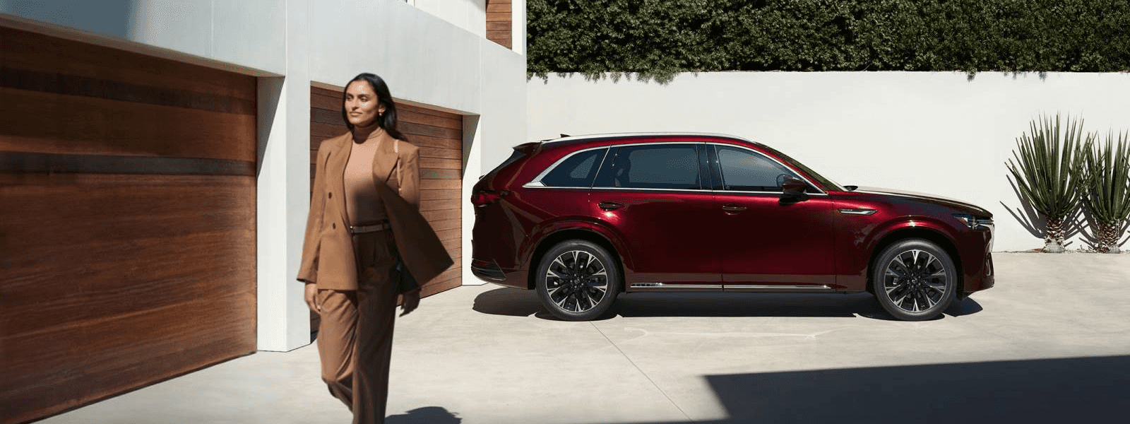 Red Mazda CX-90 parked outside a modern home with a person walking past garage doors in daylight