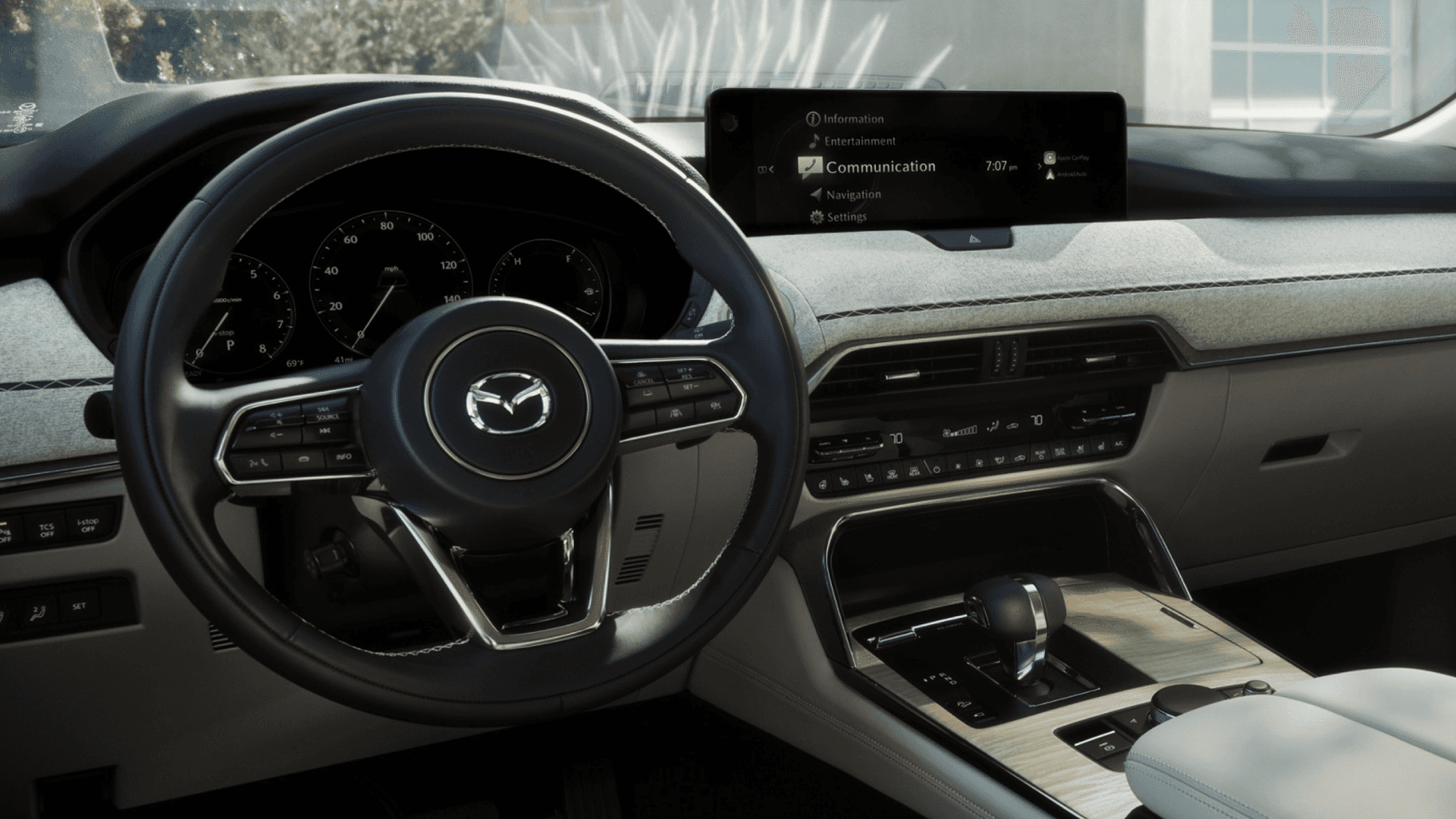 Close view of steering wheel, analog gauges, center display, climate controls, and light dashboard trim