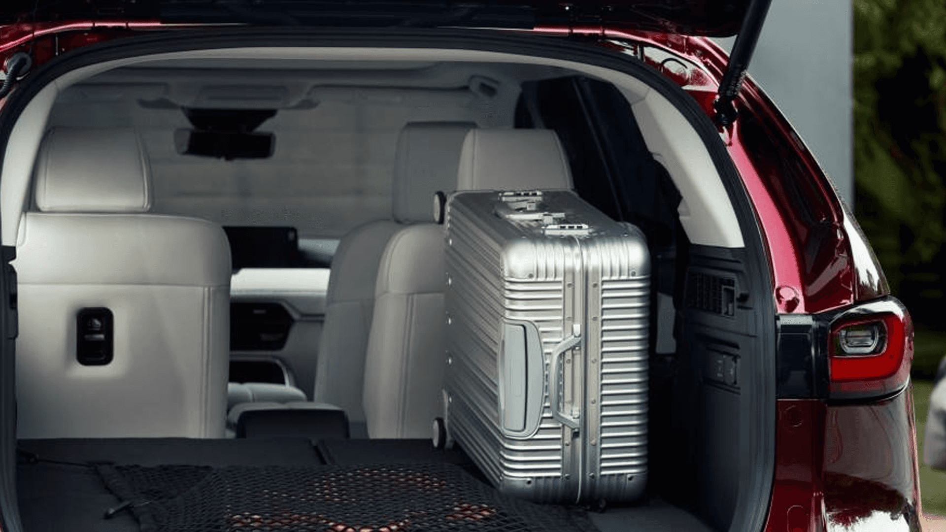 Open rear cargo area with an upright silver suitcase, folded cargo floor panel, and light rear seatbacks