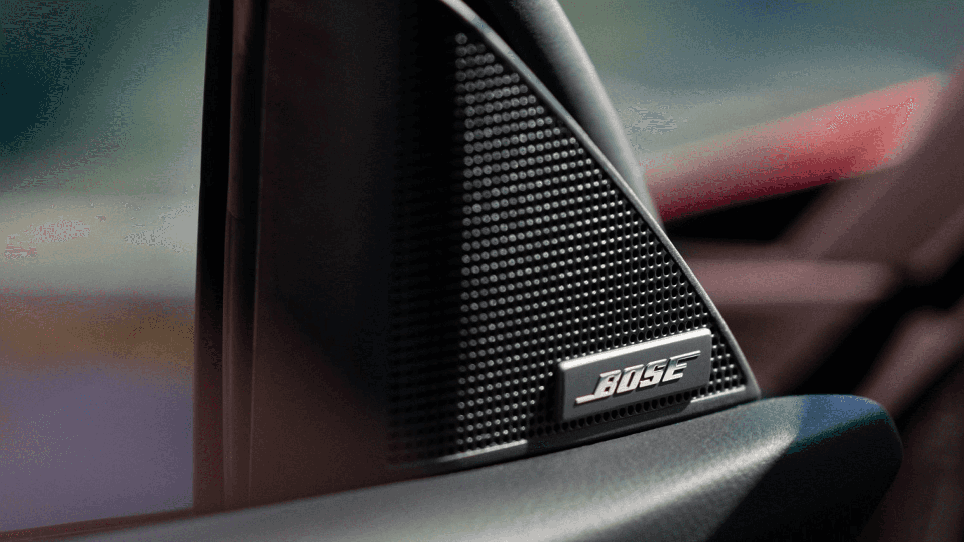 Close-up of a Bose speaker grille mounted on interior trim with a blurred red and dark background