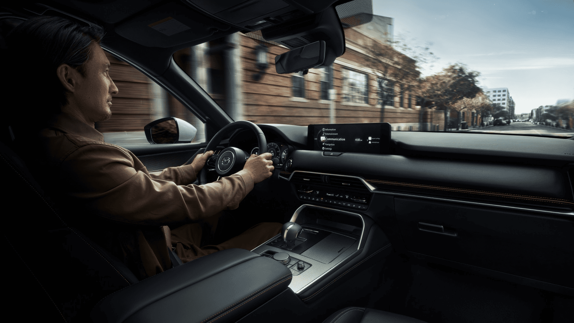 Wide cabin view with driver at the wheel, center display, black dashboard, and front console in motion