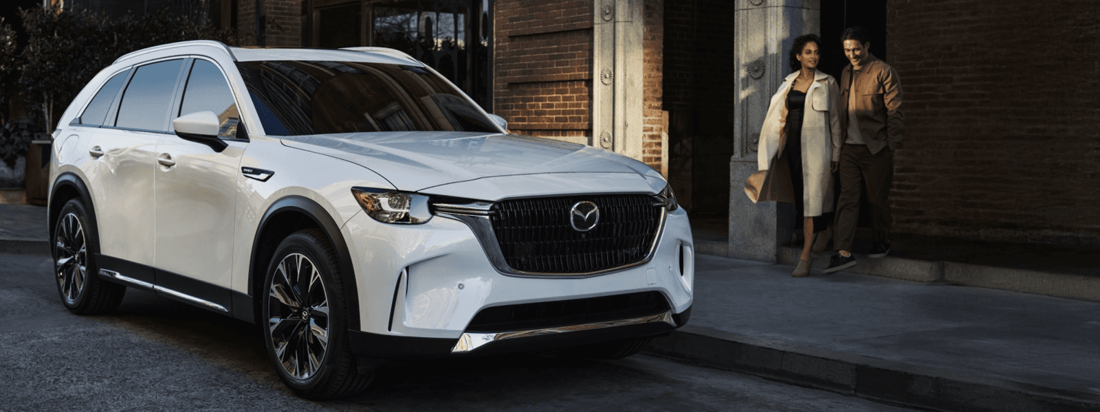 Side profile view of a white 2026 Mazda CX-90 parked near a modern home