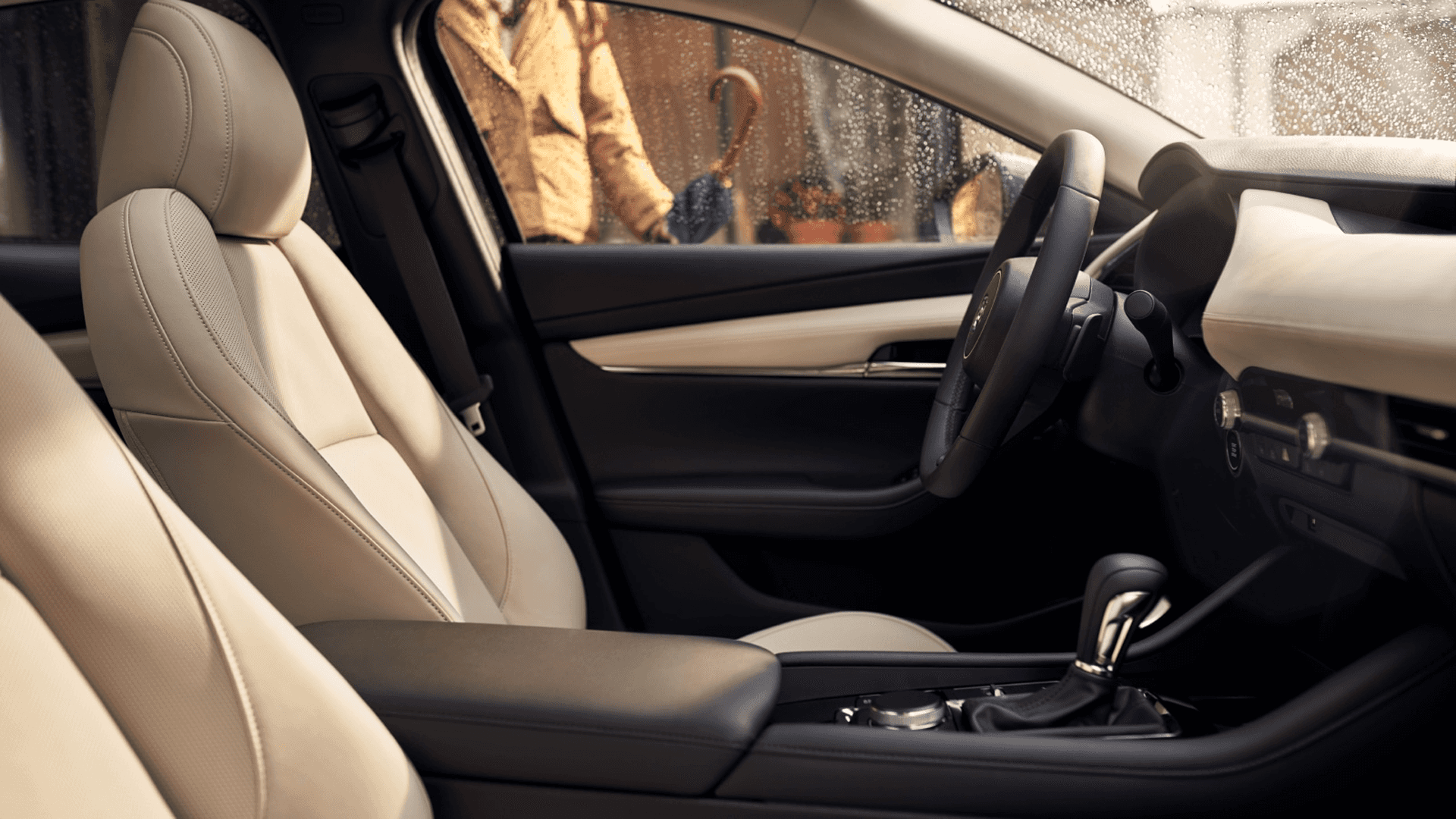 Front cabin with light seats, black console, steering wheel, and rain-speckled side window with person outside