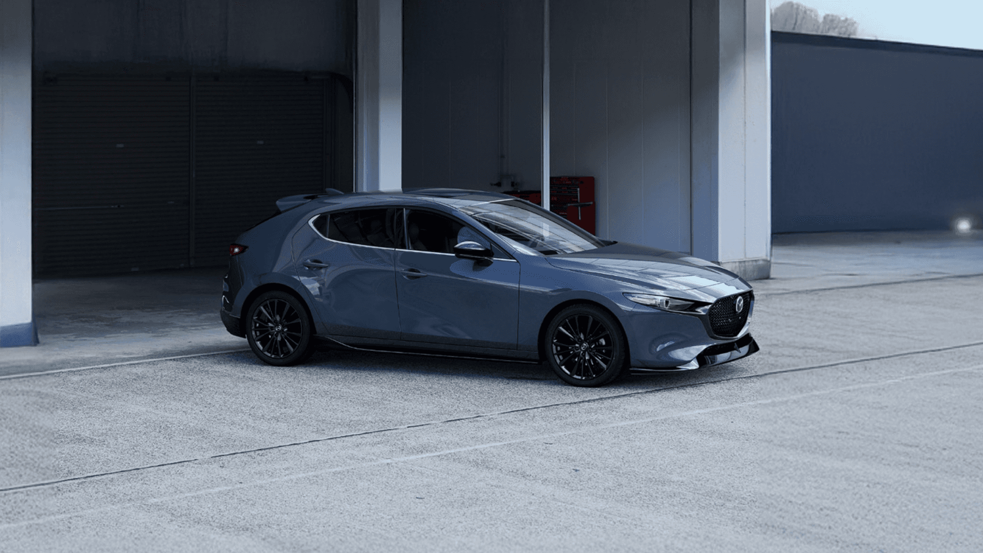 Gray hatchback parked on a concrete drive outside a modern building with tall white walls and dark garage doors