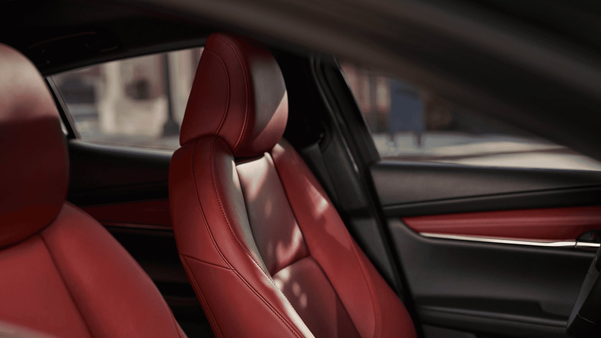 Close view of front seat in Mazda3 with red leather upholstery, visible stitching, and door panel with matching trim