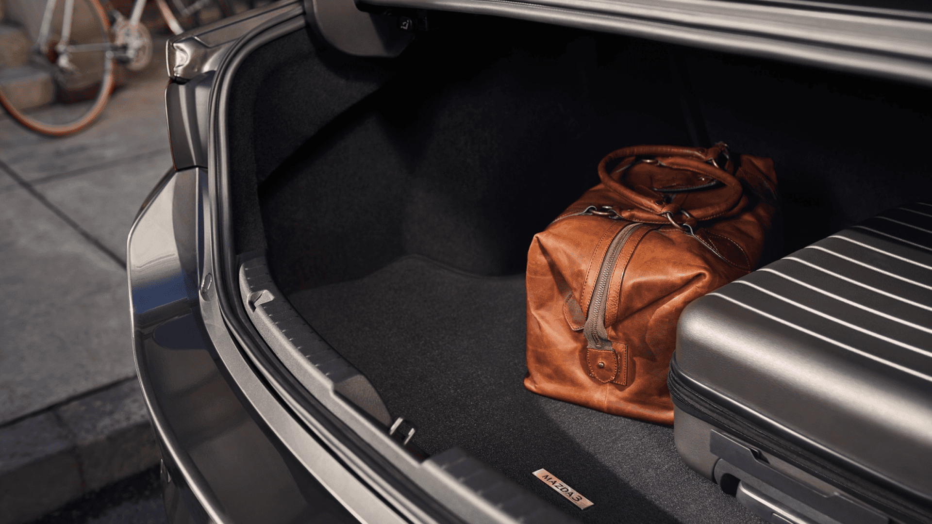 Open Mazda3 trunk showing luggage and duffel bag inside cargo area with wide opening and interior lining visible